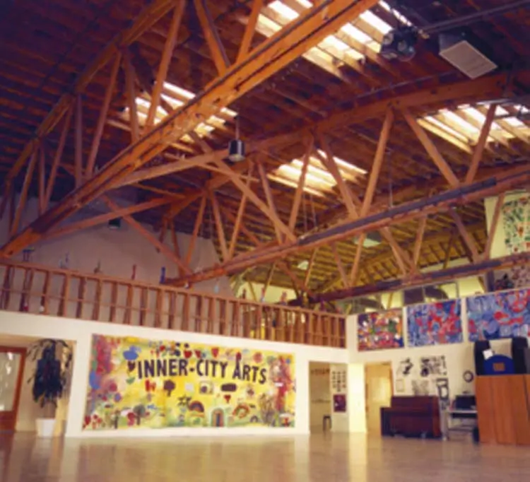 Open studio under exposed timber trusses and skylights with a colorful Inner-City Arts mural