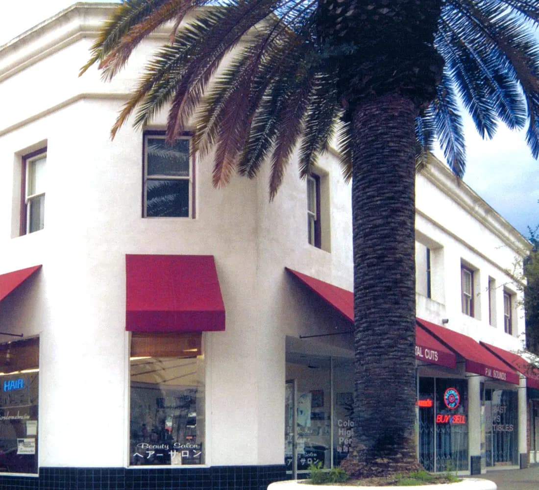 Corner of the restored Blair House building with red awnings and a tall palm in Old Torrance